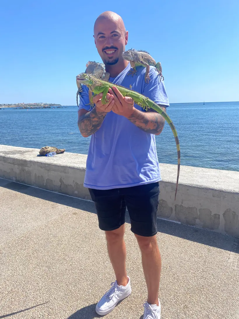Adrian an einer Uferpromenade am Meer, mit drei Leguanen auf Armen und Schultern