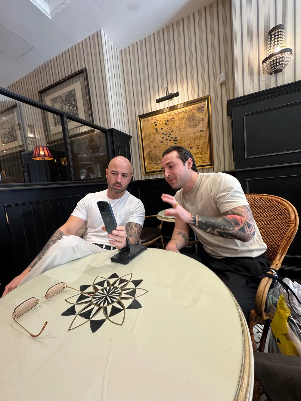Adrian im Gespräch mit einem Freund im Café, beide schauen aufs Handy